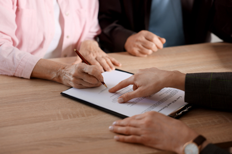 Notary showing senior couple where to sign Last Will and Testament at wooden desk in office, closeup
